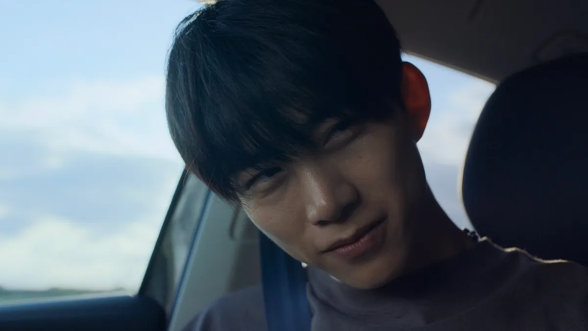 Hwang smiling softly inside a car during a quiet moment