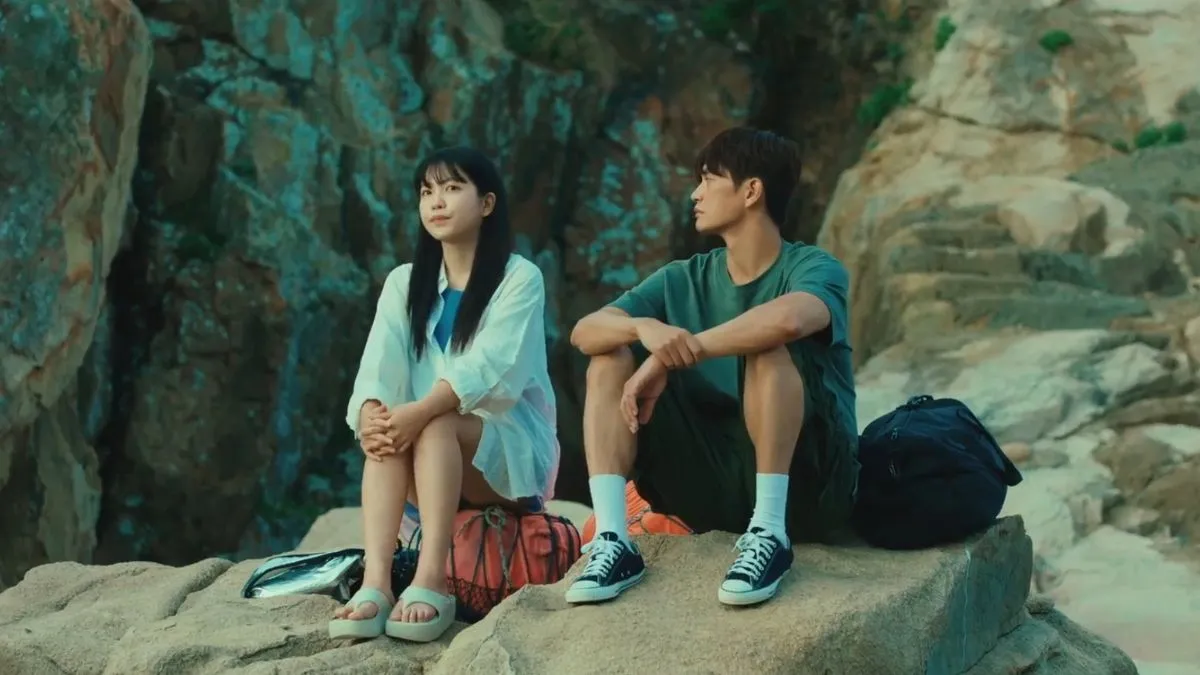 An Na and Deok Hyeon sitting on a rugged, rocky cliffside.