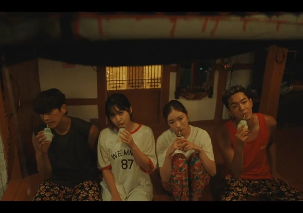 An Na and Deok with their friends sitting side-by-side inside a dimly lit room