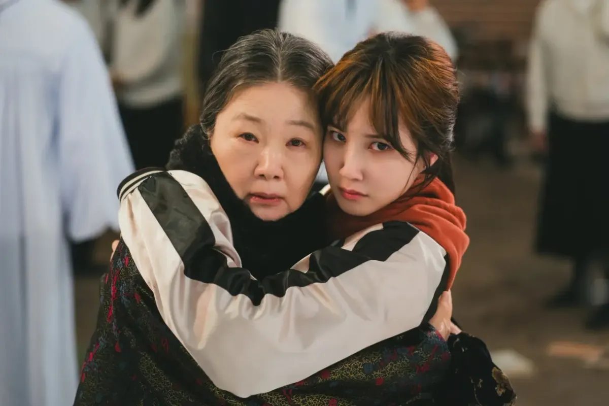The WONDERfools scene of Eun Chae-ni embracing her grandmother in a varsity jacket, both looking emotional amid a crowd of onlookers.