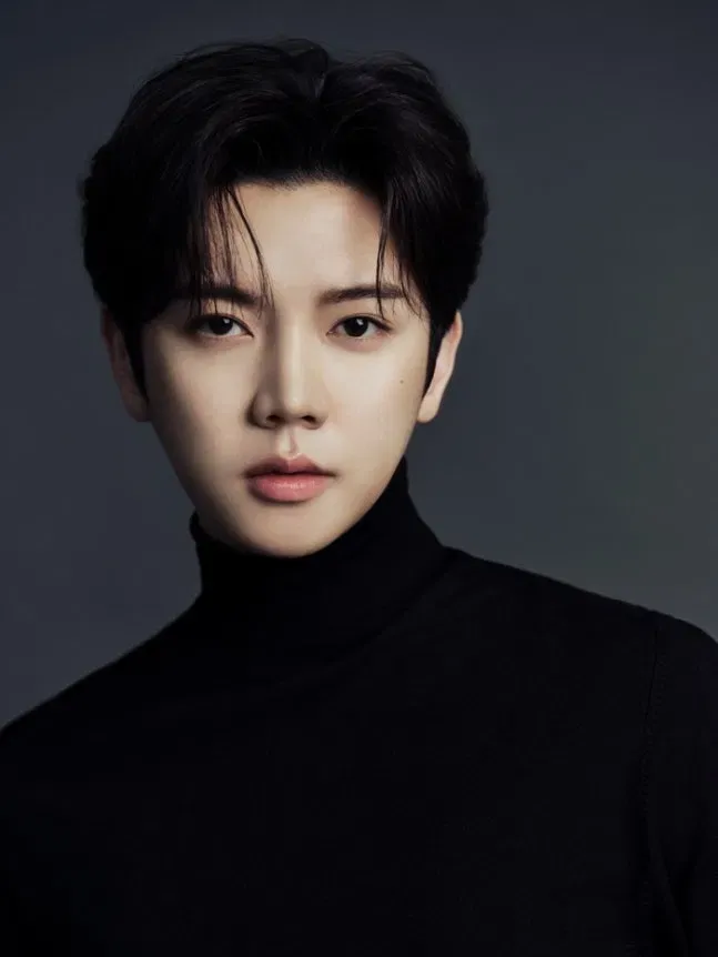 Ren, former NU'EST member, close-up professional portrait in a black turtleneck against a dark grey background.