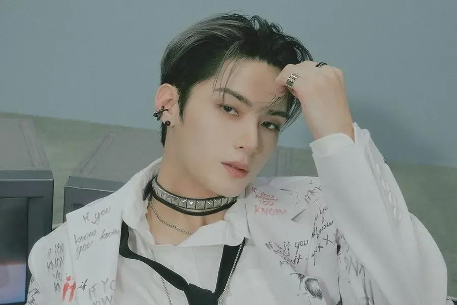 Hangyeom of OMEGA X with dark tousled hair and a studded choker, wearing a graffiti-print white shirt, posing for a concept photo.